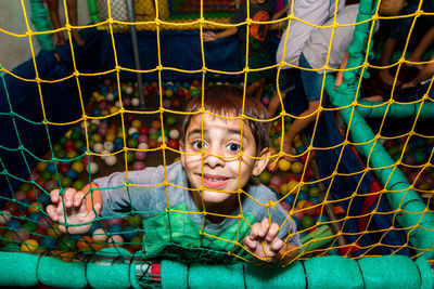 High angle portrait of happy boy playing with balls seen through netting