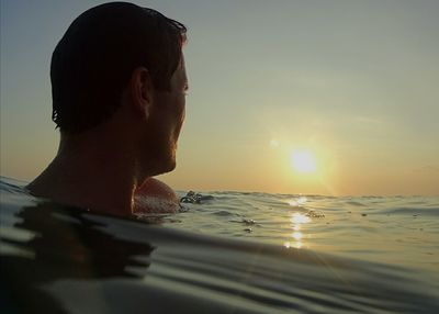 Man swimming in sea against sky during sunset