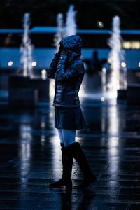 Woman wearing jacket standing against fountain