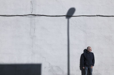 Adult man standing against white wall with shadow of street lamp