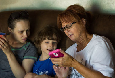 Mother showing mobile phone to daughters while sitting on sofa at home