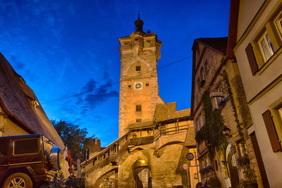 Low angle view of clock tower amidst buildings in city against blue sky