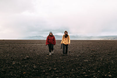 Young happy tourists in winter wear going on deserted ground and cloudy sky
