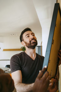 Smiling man hanging frame on wall at new home