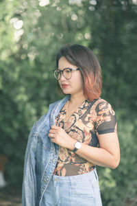 Beautiful young woman standing by plants against trees