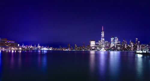 Illuminated buildings by sea against sky at night