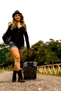 Low angle view of beautiful woman pulling luggage while walking on dirt road