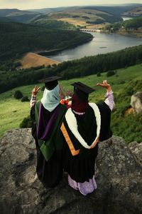 Rear view of female friends in graduation gowns standing on mountain