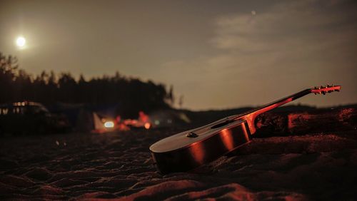 Close-up of guitar on illuminated land against sky at sunset
