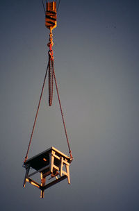 Low angle view of table hanging from crane against sky