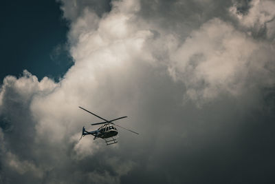 Low angle view of helicopter flying against cloudy sky