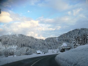 Snow covered road by trees against sky