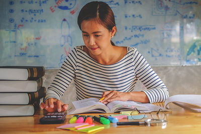 Woman studying at desk against whiteboard