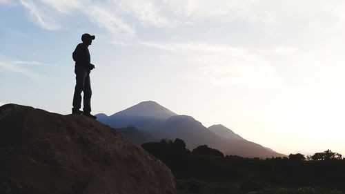 Silhouette man standing on rock against sky