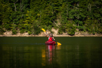 Woman rowing boat on lake against trees