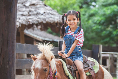 Portrait of cute smiling girl sitting on pony at farm