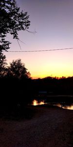 Silhouette trees by lake against sky during sunset