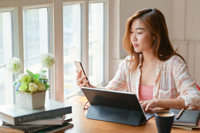 Young woman using phone while sitting on table