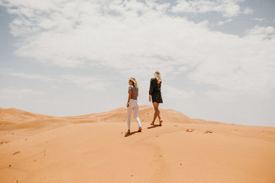 People on sand dune in desert against sky