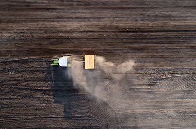 A tractor is plowing a dusty field on a windy day. a group of seagulls is controlling the work.