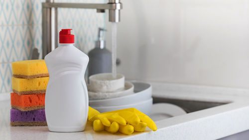 A white bottle with dishwashing gel, sponges and rubber gloves 