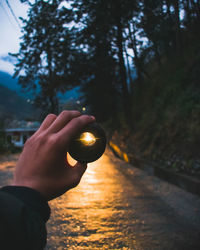 Cropped hand holding lens against illuminated road at dusk