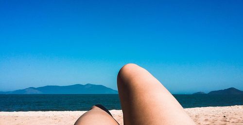 Low section of woman relaxing on beach against sky