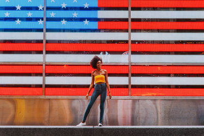 Full length portrait of happy young woman standing against neon american flag in city