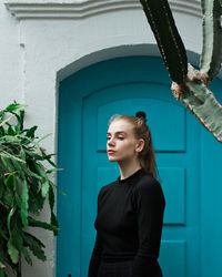 Young woman standing against blue door