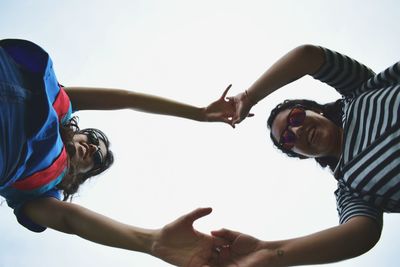 Directly below shot of female friends holding hands against clear sky