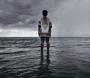 Rear view of man standing at beach against sky