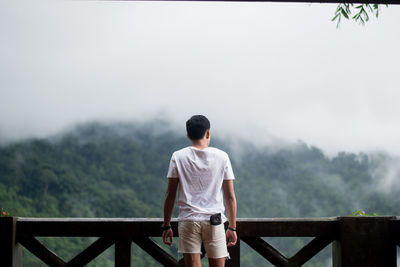 Rear view of man standing on railing against mountain