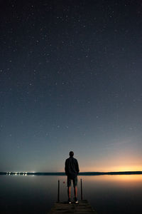 Rear view of man standing on pier over sea against sky at night