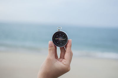 Close-up of hand holding clock at beach against sky