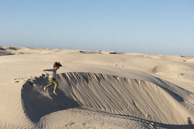 Man on sand dune in desert against clear sky