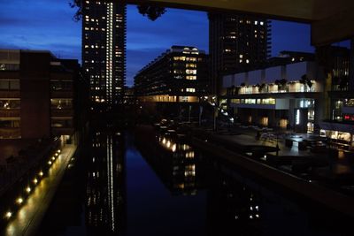 Illuminated bridge over river by buildings in city at night