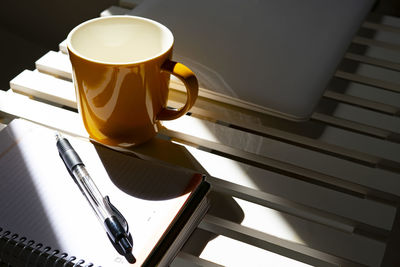 Yellow cup of coffee on a desk with a calendar and a pen.