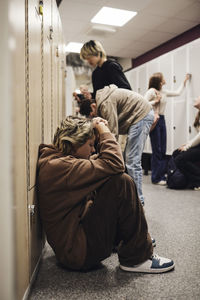 Side view of depressed teenage girl sitting by locker in school corridor