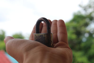 Close-up of person holding padlock against sky