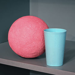 Pink papier mache ball and blue plastic cup on the shelf - geometric design with space for copy.