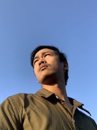 Portrait of young man looking away against clear blue sky