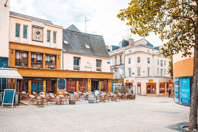 Chairs and tables by buildings in city against sky