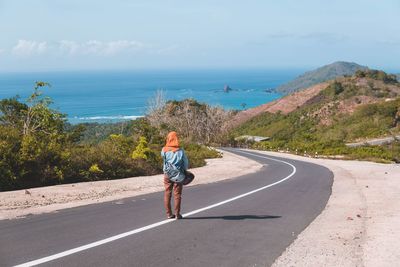 Rear view of woman on road by sea against sky