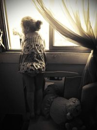 Rear view of young woman standing on bed at home