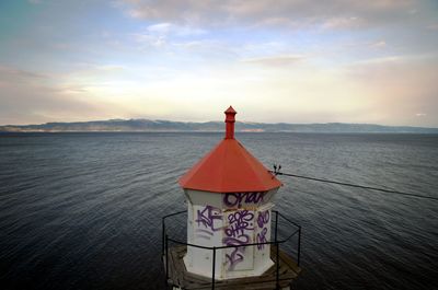 Lighthouse by sea against sky during sunset