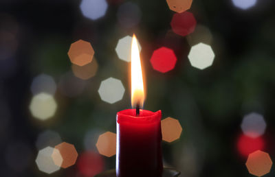 Close-up of lit candle against christmas tree lights in background