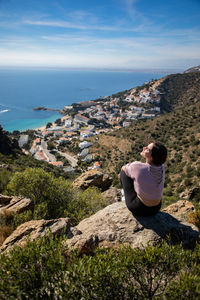 Woman sitting on rock against townscape and sea