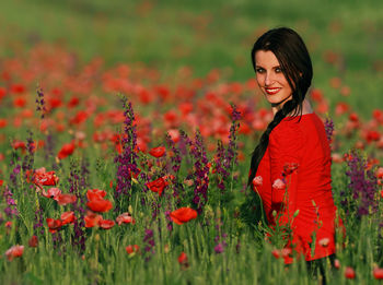 Portrait of young woman with red poppy flowers in field