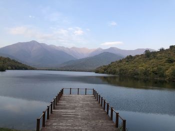 Pier on lake by mountains against sky