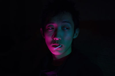 Close-up of young man eating lollipop against black background